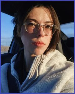 Young person in a cozy jacket gazes thoughtfully from a car with a serene sky backdrop.